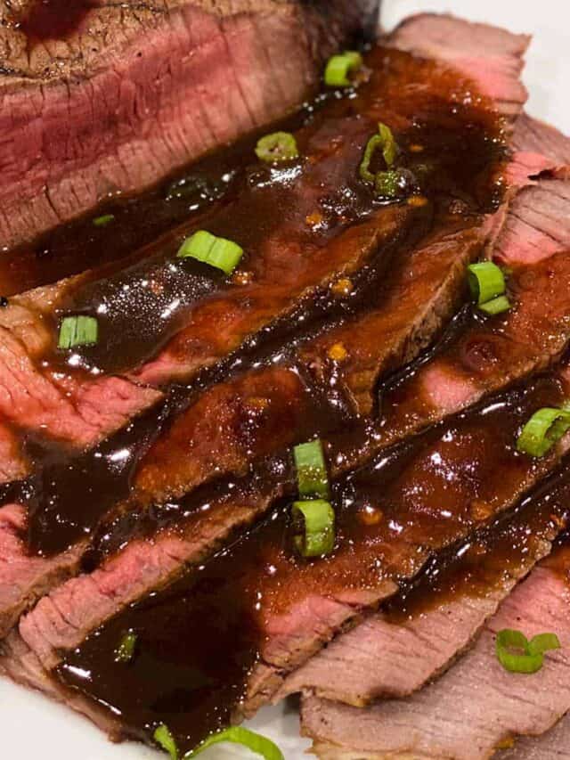 Slices of grilled london broil covered in sauce and green onions