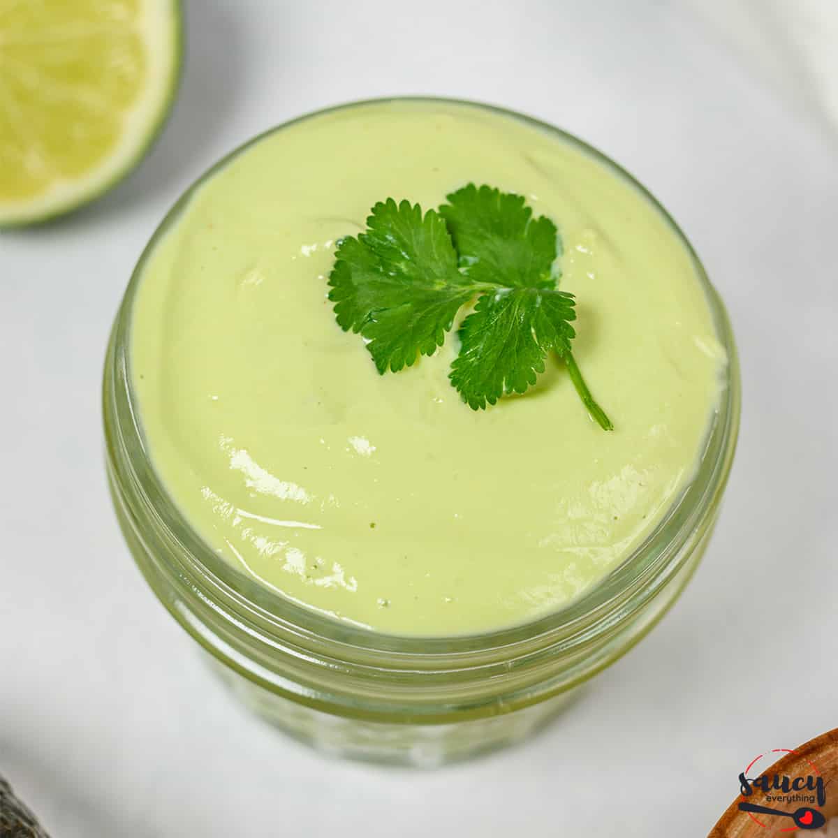 Smooth avocado crema in a glass jar with a piece of cilantro on top