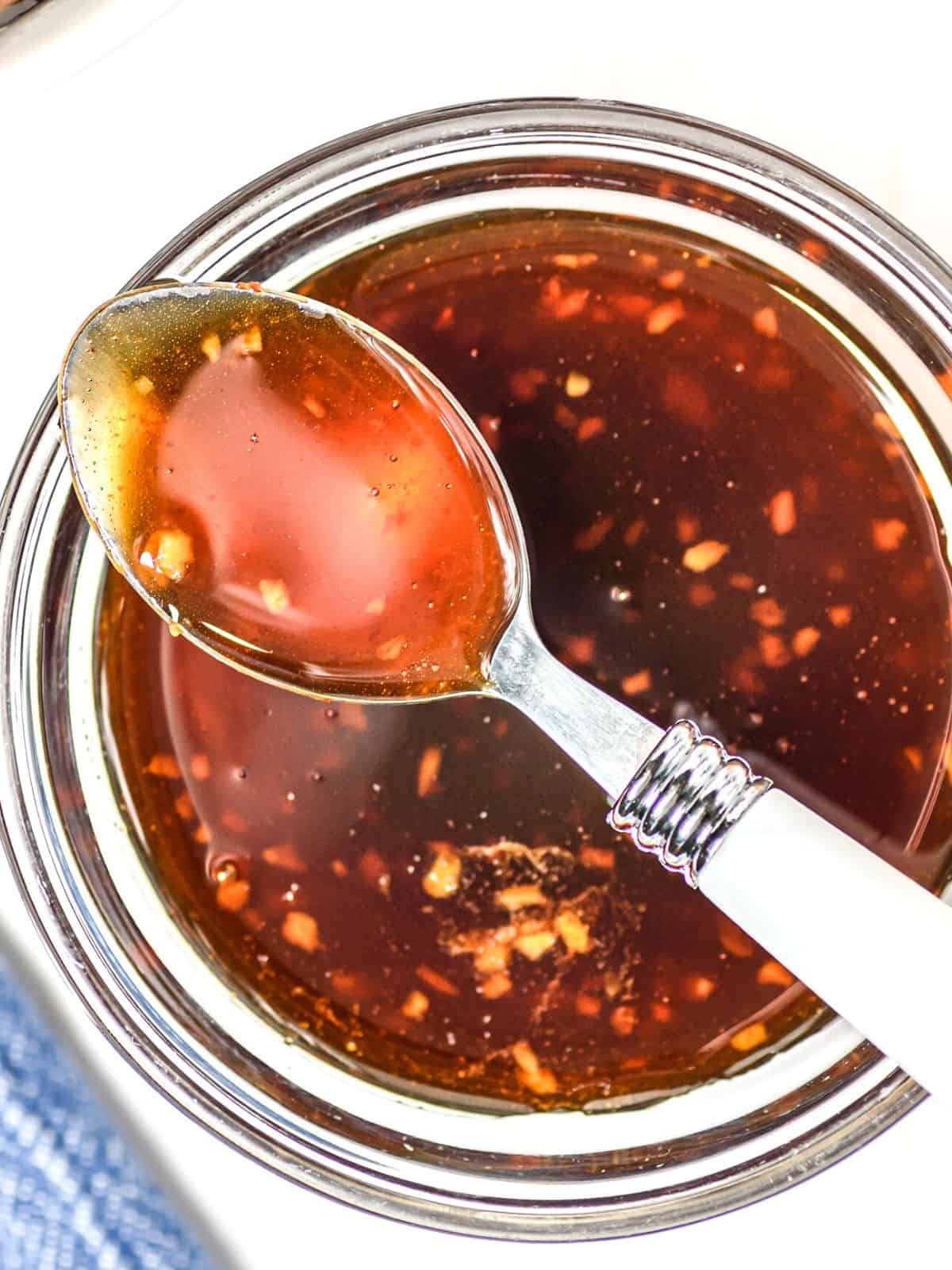 Spoon of honey sriracha sauce over a glass bowl of sauce