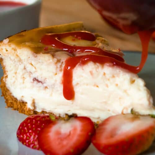 Cheesecake slice on plate with strawberry sauce drizzled on