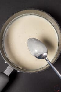 Creamy garlic sauce with a spoon in a sauce pan