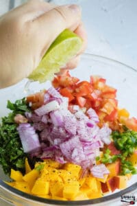 Squeezing lime over peach salsa with mango