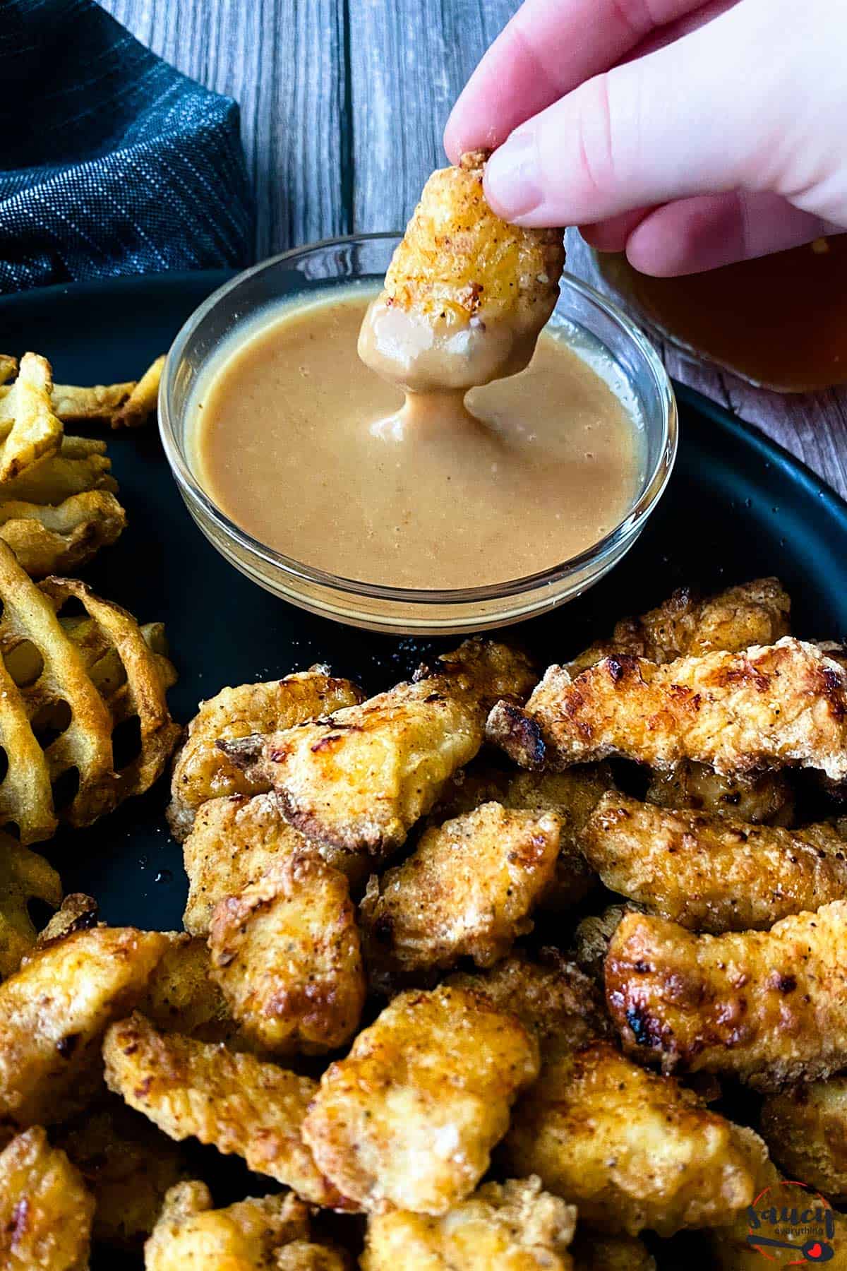 Chick-fil-a sauce in a bowl next to nuggets and waffle fries, dipping a nugget in the sauce