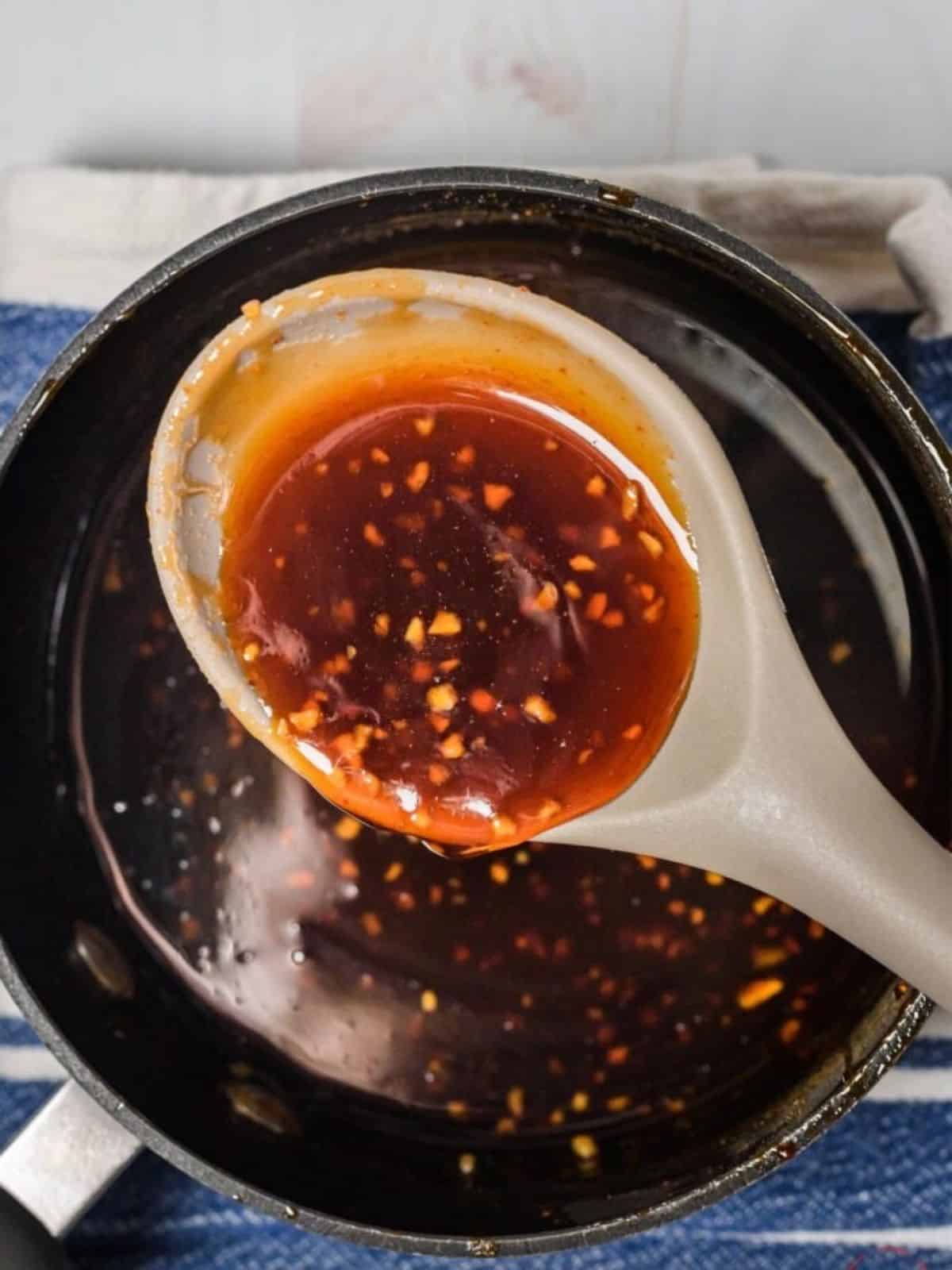 Honey Sriracha sauce in a skillet being picked up by a spoon.