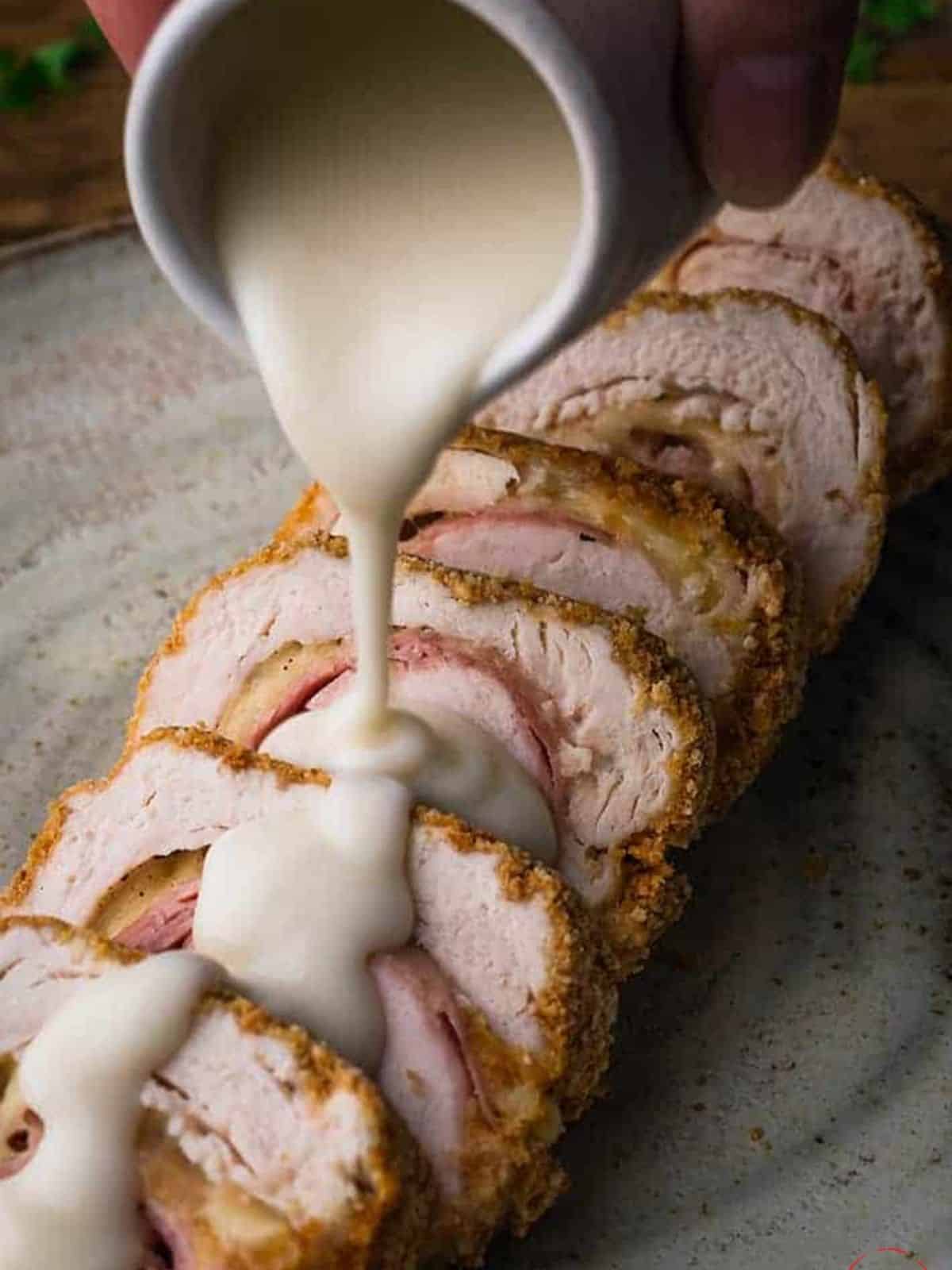 White parmesan sauce being poured over sliced chicken.