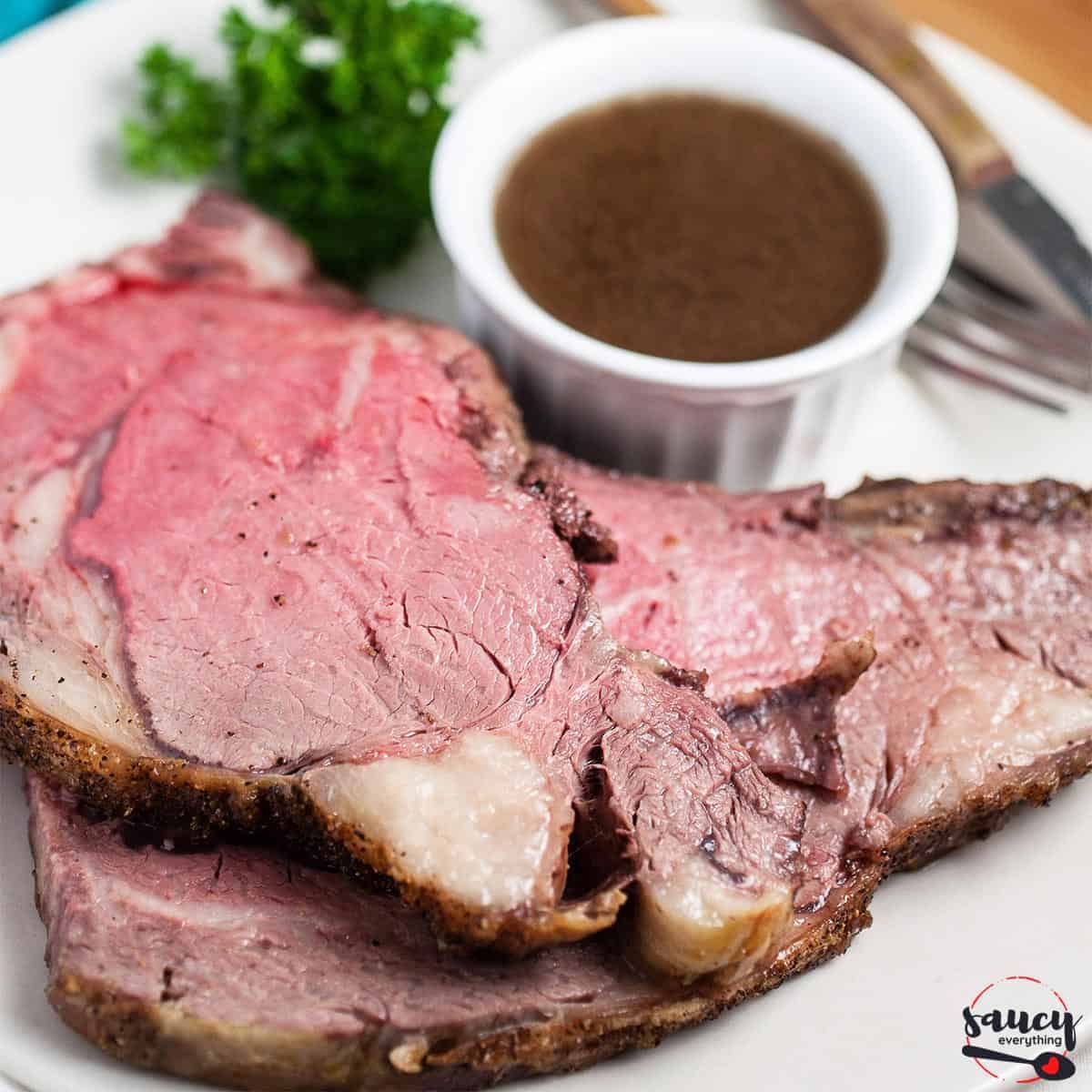 au jus sauce in a bowl next to two slices of prime rib