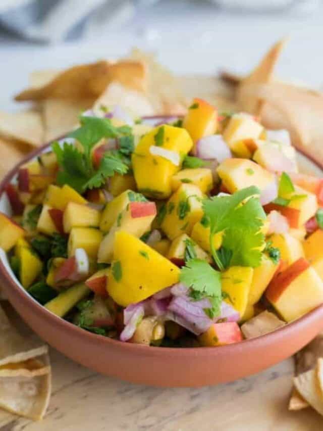 Peach salsa in a bowl surrounded by tortilla chips.