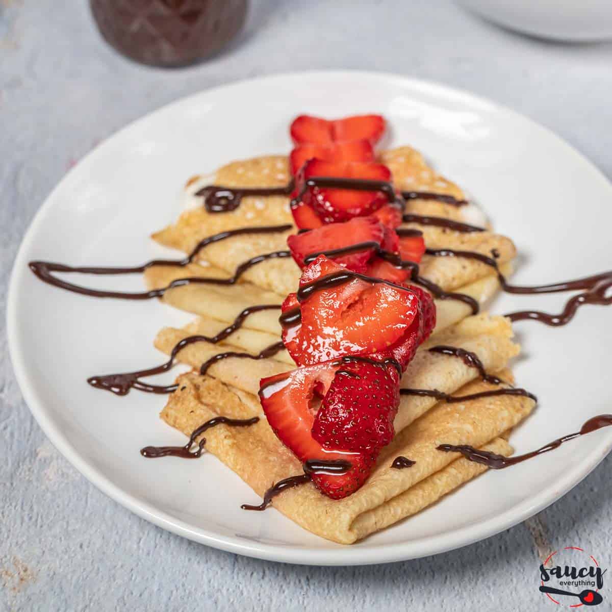 Chocolate sauce drizzled over crepes with strawberries on a plate