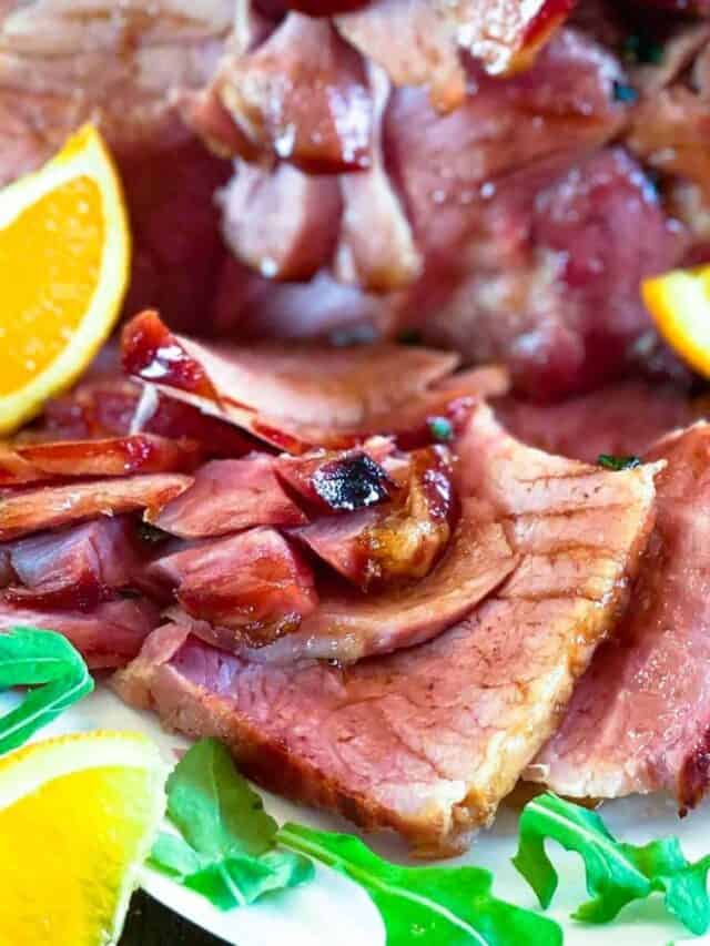 Sliced ham with orange wedges with ham glaze on top.