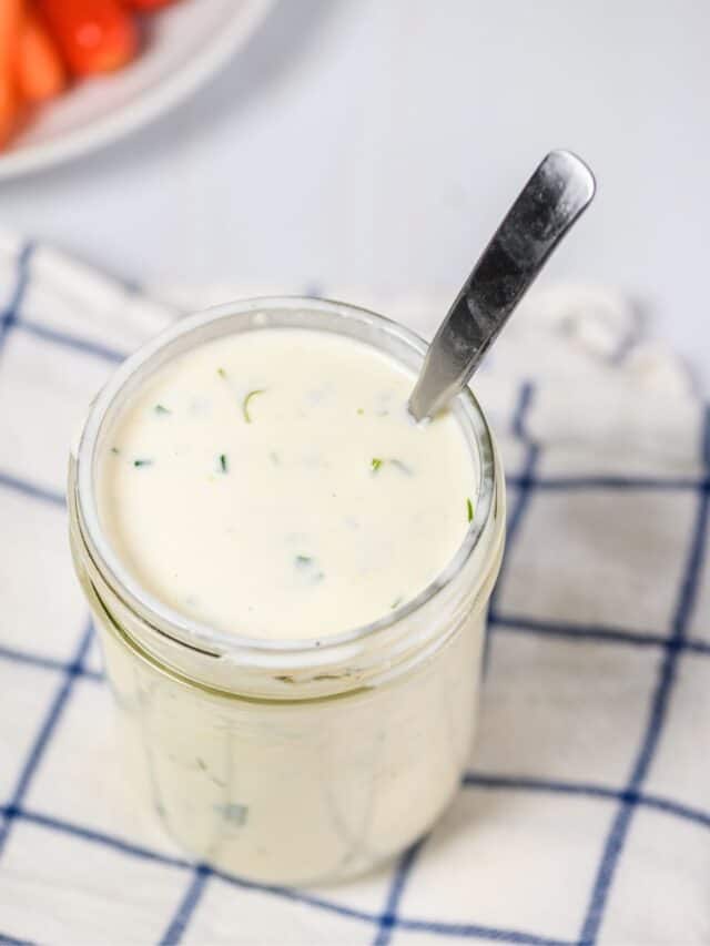 Ranch dressing in a glass jar with a spoon inside.