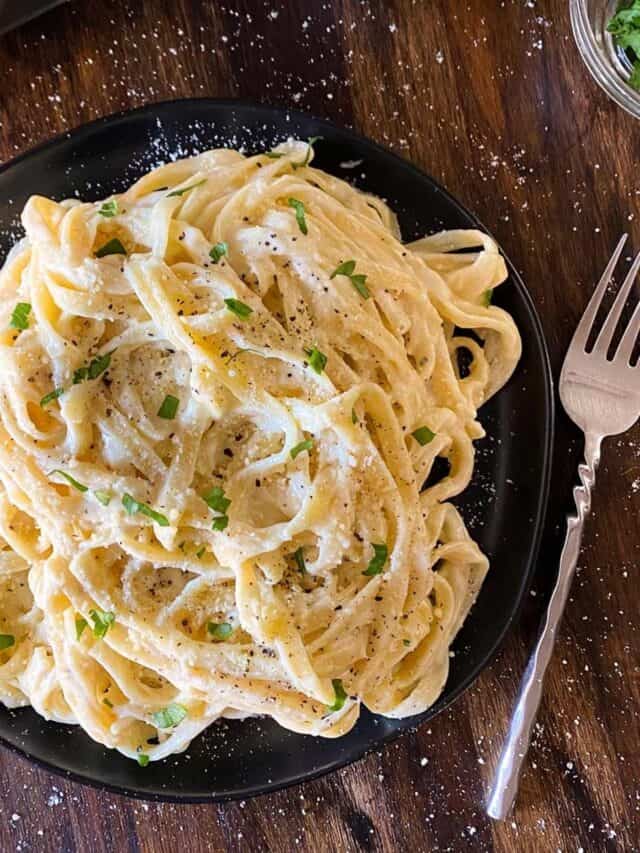 Fettuccini noodles on a plate topped with Alfredo sauce.
