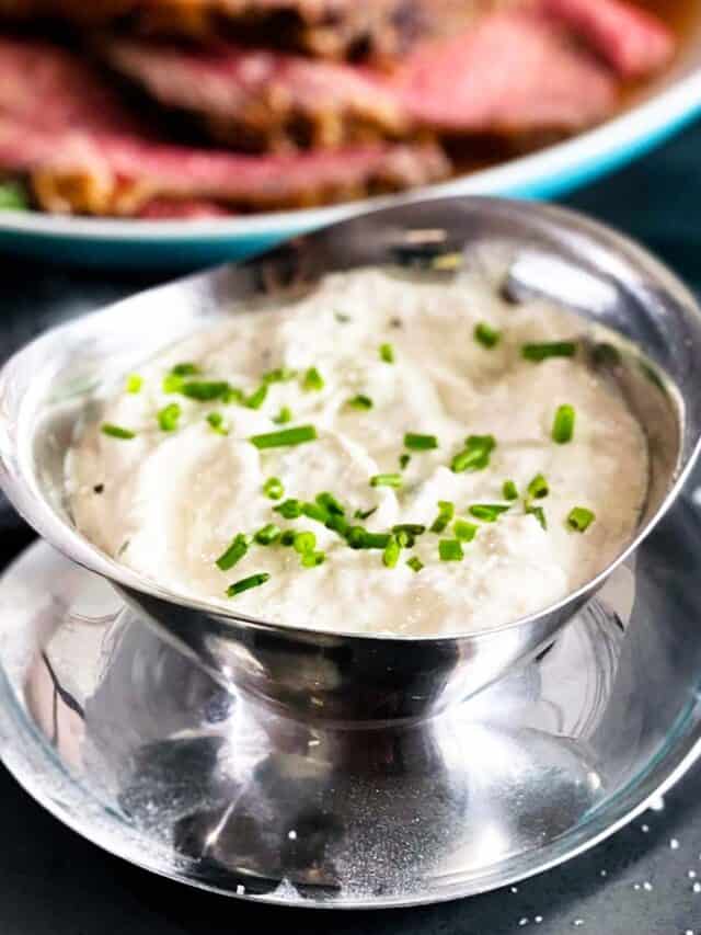 Horseradish sauce in a silver serving bowl with chives next to a big plate of prime rib
