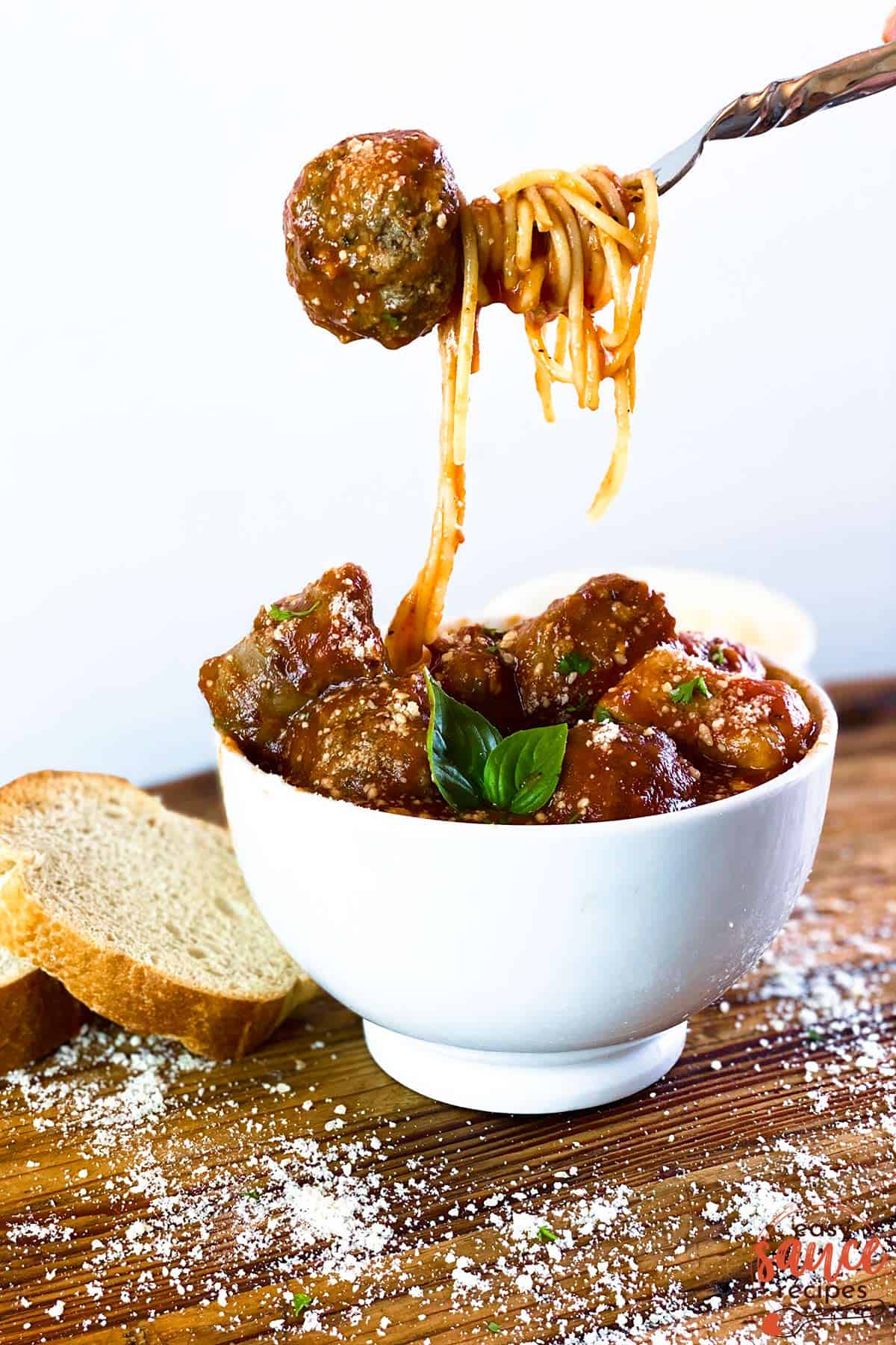 holding a meatball over a bowl of meatballs with sauce and pasta