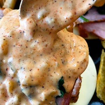 Spooning remoulade sauce onto a philly pork sandwich