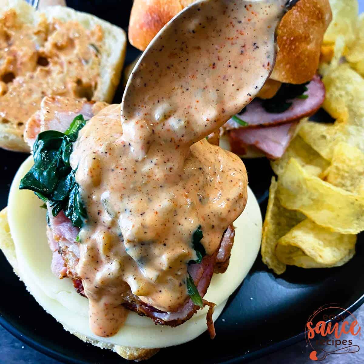 Spooning remoulade sauce onto a philly pork sandwich