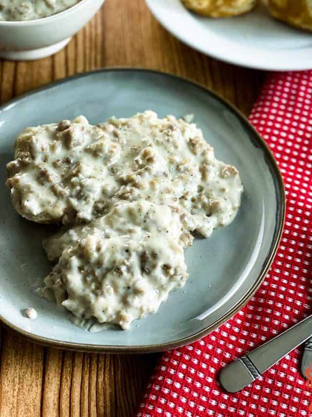 Sausage gravy on three biscuits on a plate with a fork and red napkin
