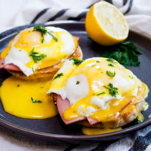 hollandaise sauce poured over eggs benedict on a black plate