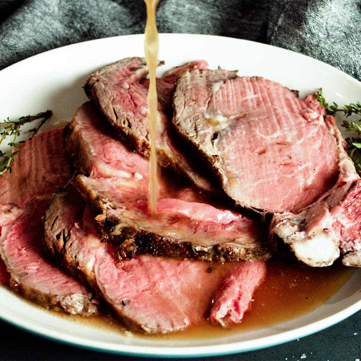 Pouring au jus over sliced prime rib on a white plate