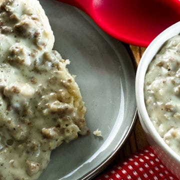 Sausage gravy over biscuits on a plate next to a bowl of gravy