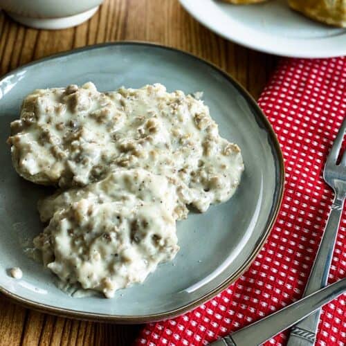 Sausage gravy on three biscuits on a plate with a fork and red napkin