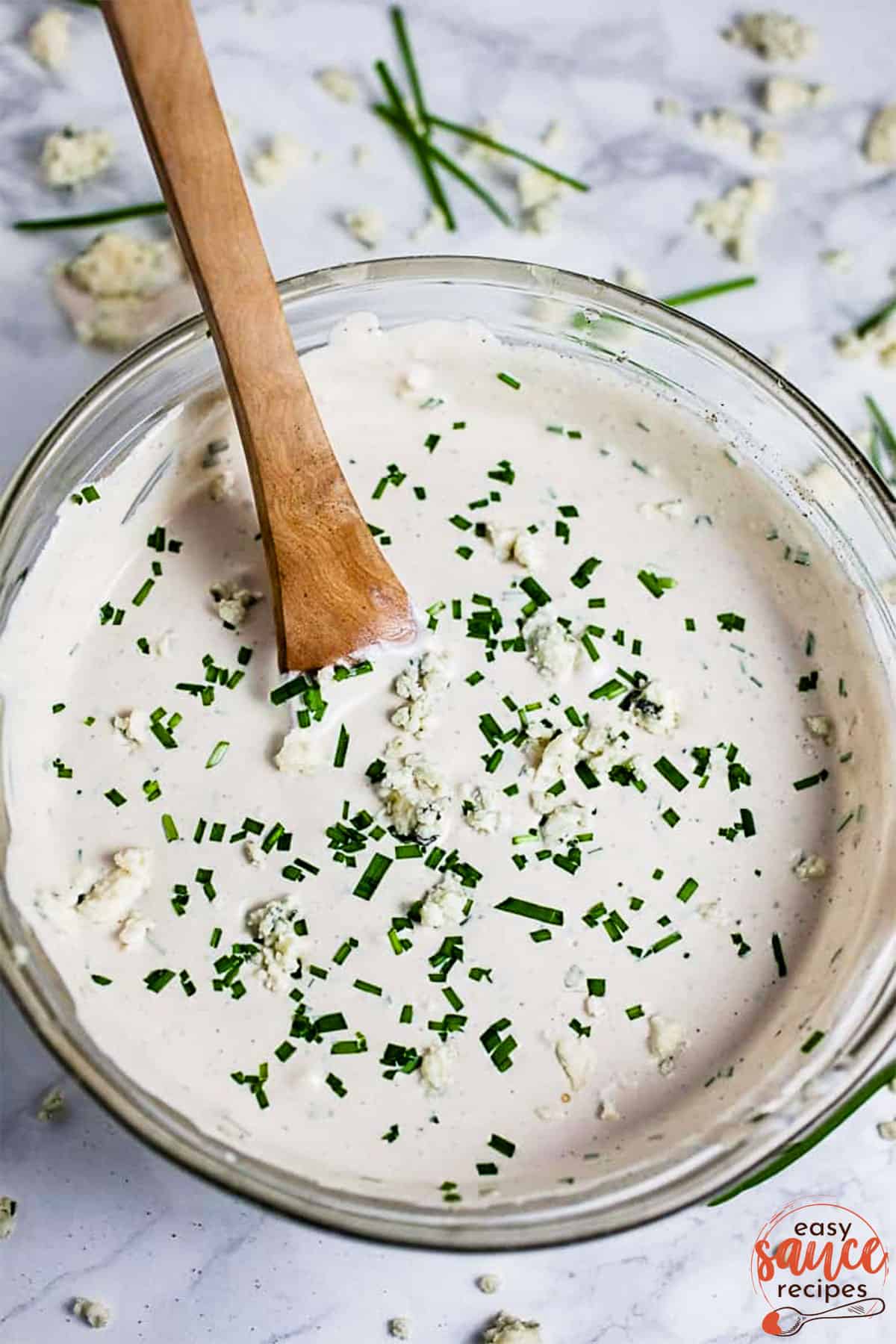 Blue cheese dressing with chives in a bowl with a wooden spoon