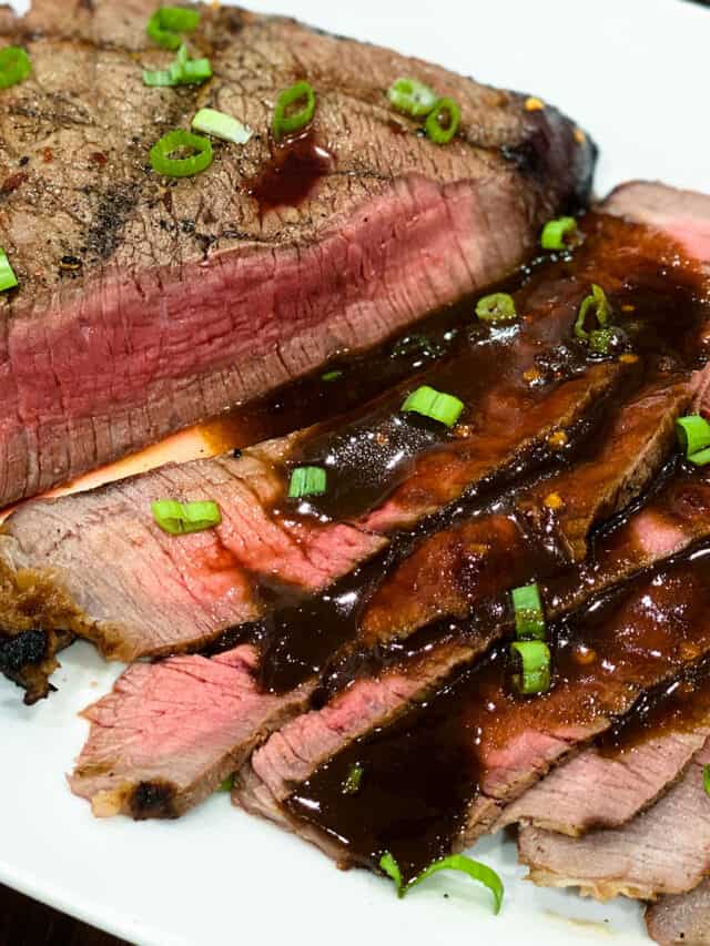 Slices of grilled london broil covered in sauce and green onions