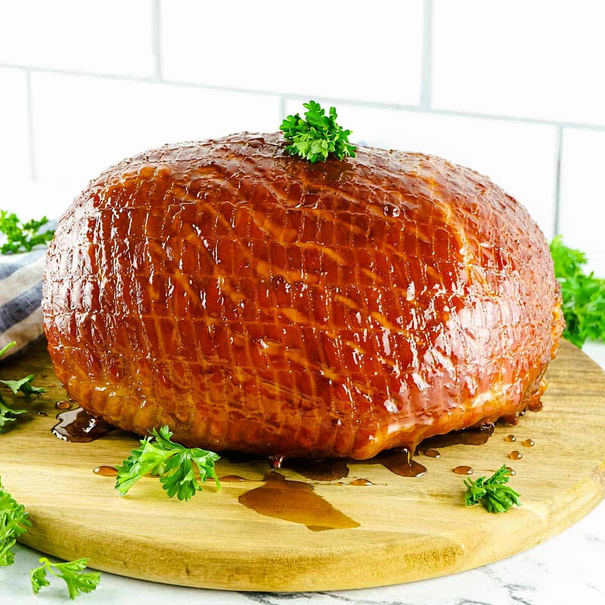 whole bourbon glazed ham on a serving board with herbs