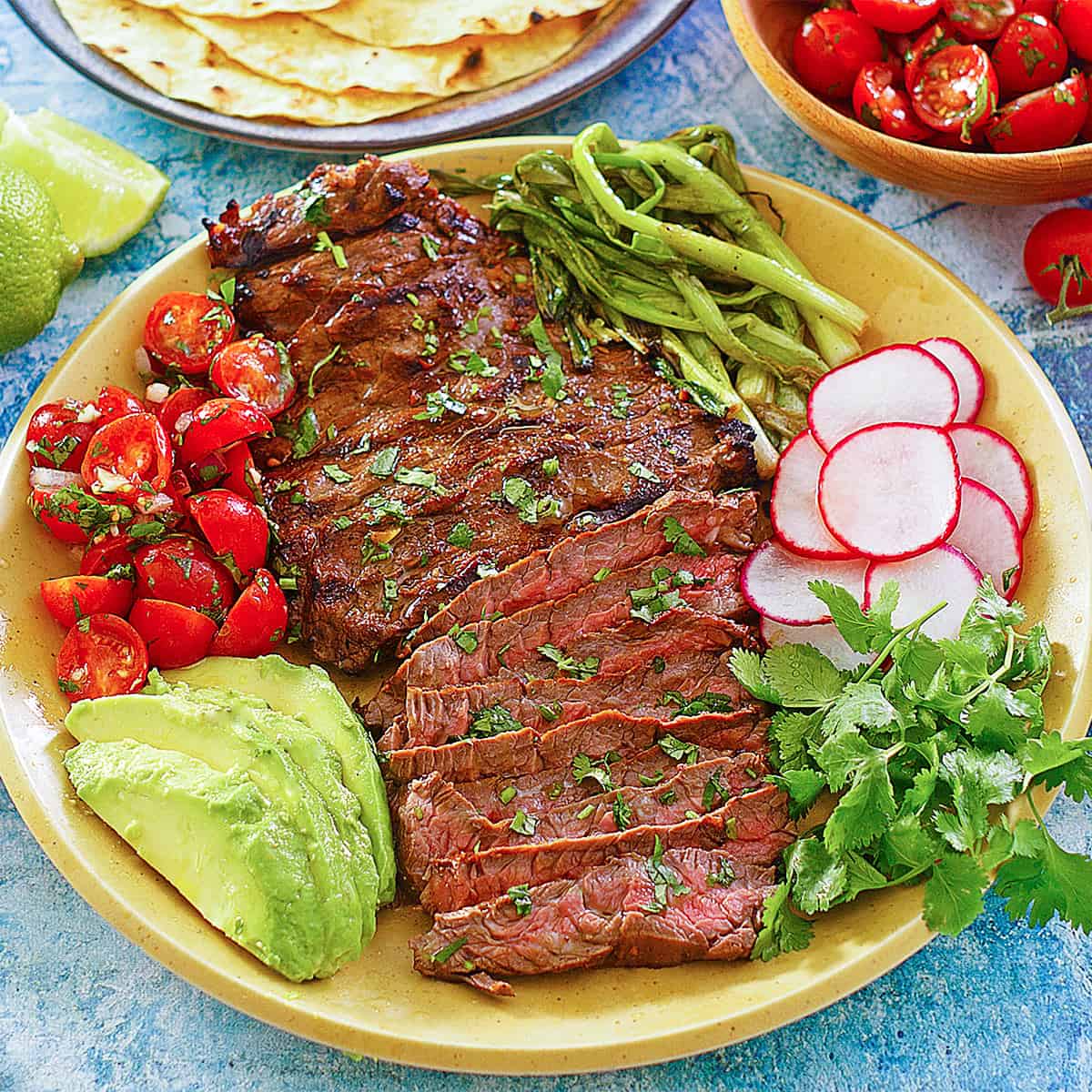 Sliced carne asada taco meat on a plate with vegetables