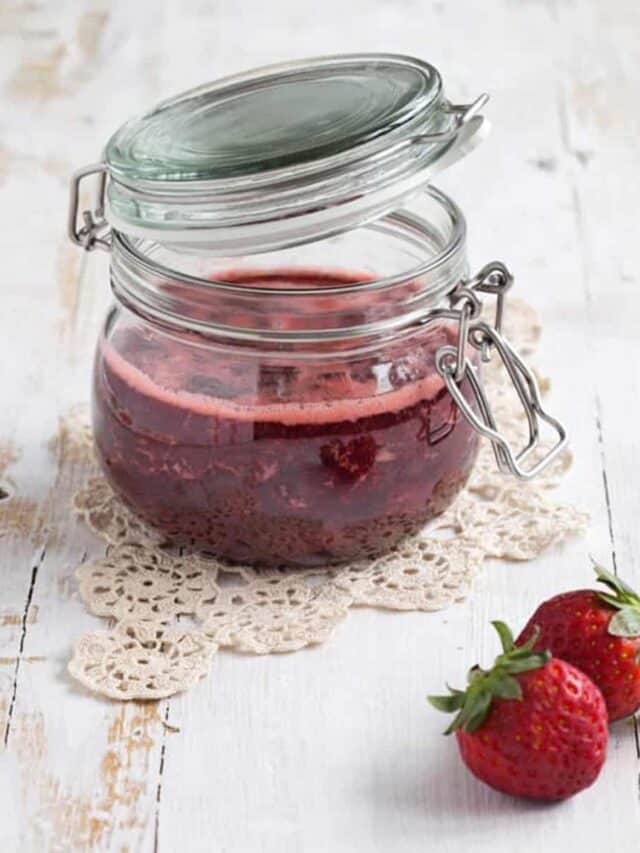 strawberry jam in a jar next to two strawberries
