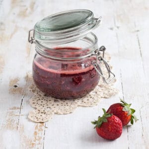 strawberry jam in a jar next to two strawberries