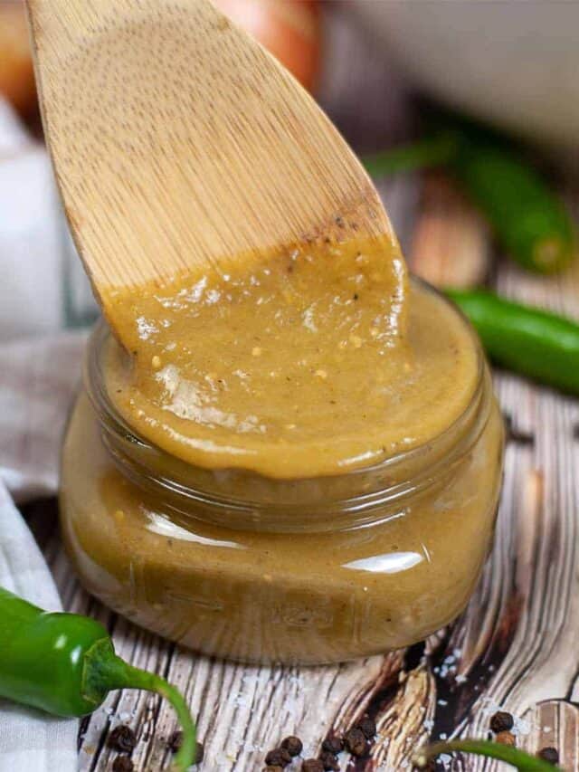 green enchilada sauce in a glass container next to jalapenos with a wooden spoon