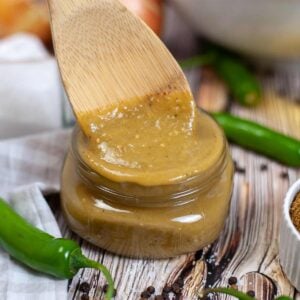 green enchilada sauce in a glass container next to jalapenos with a wooden spoon