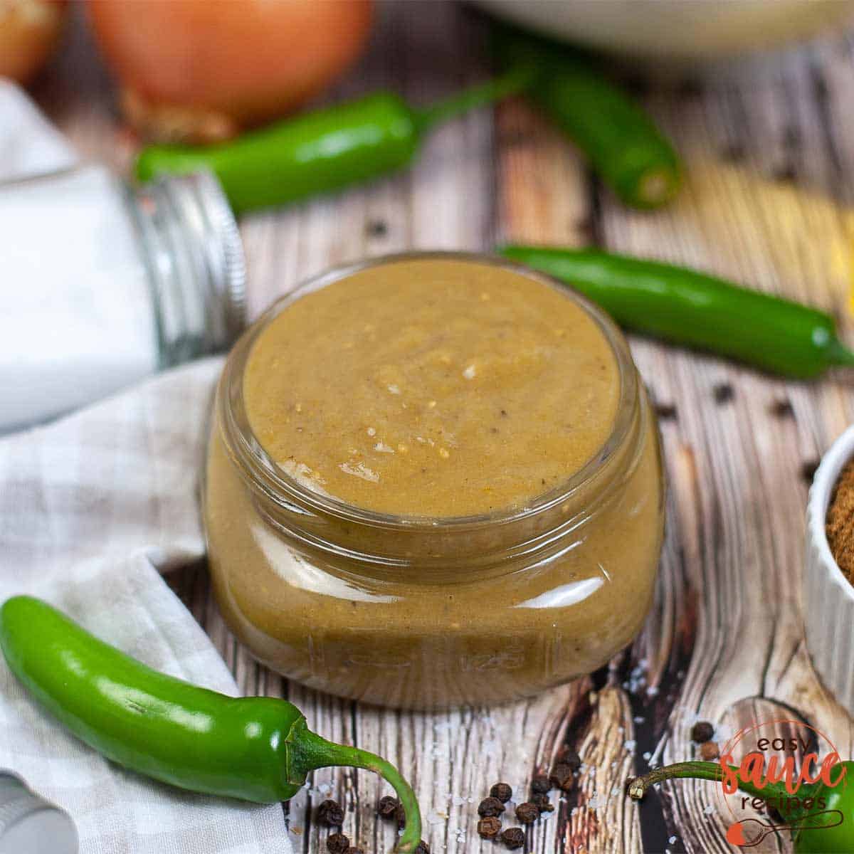 green enchilada sauce in a glass container next to jalapenos