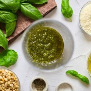 Pesto mixed in a glass surrounded by pesto ingredients