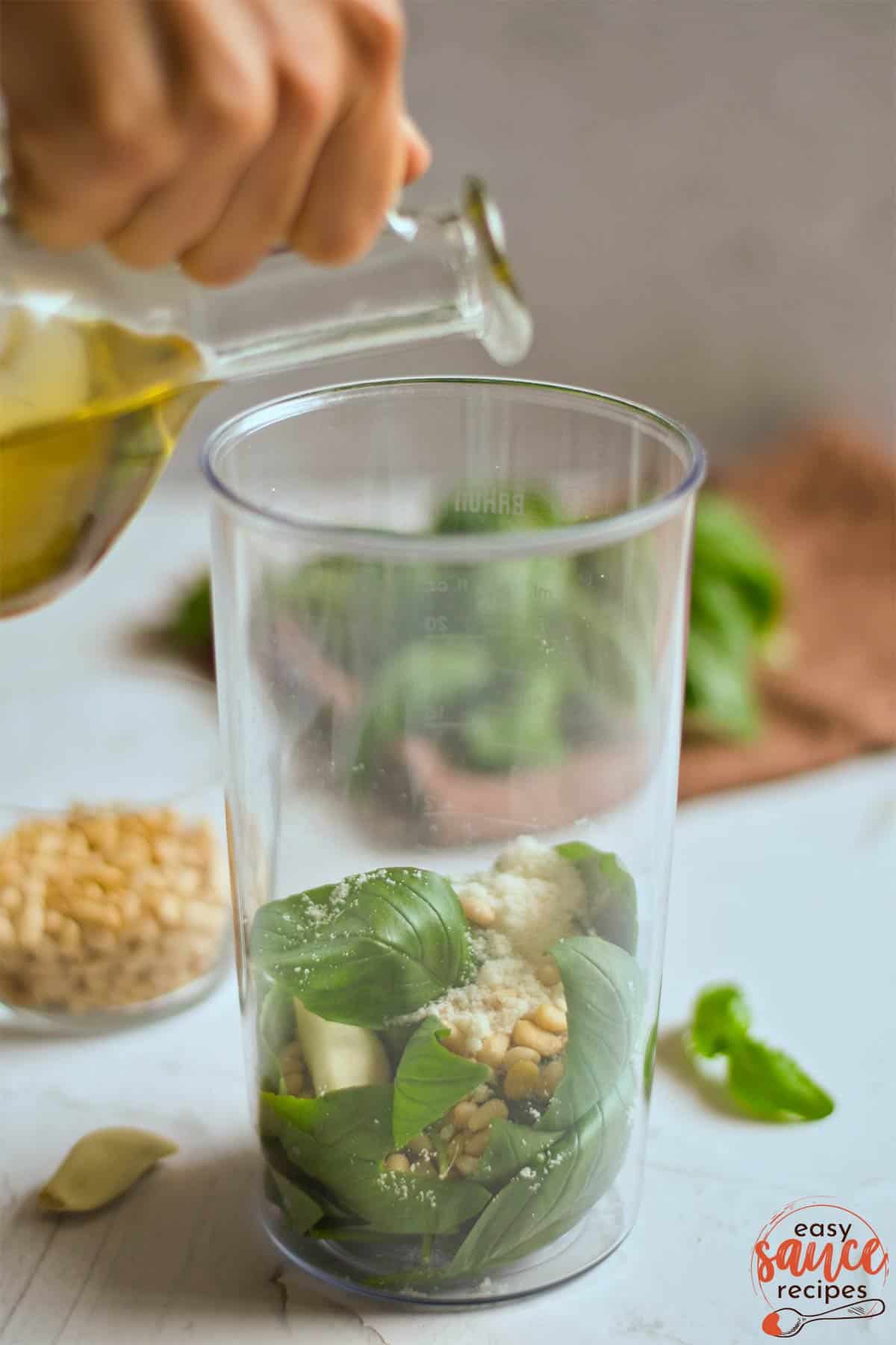 Pouring olive oil into a glass containing pesto ingredients