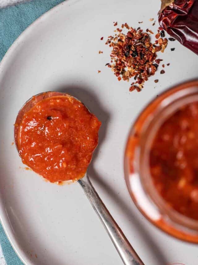 harissa sauce on a spoon placed on a white plate with red chilies