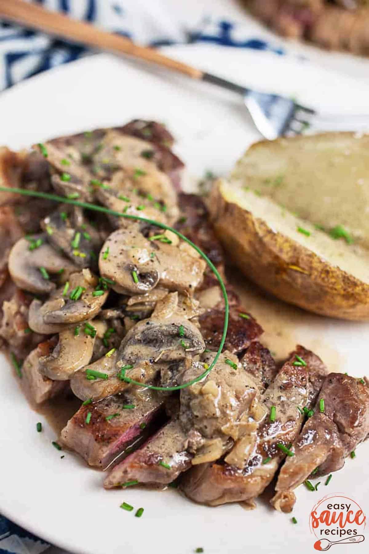 steak diane sliced on a plate with sauce and a baked potato