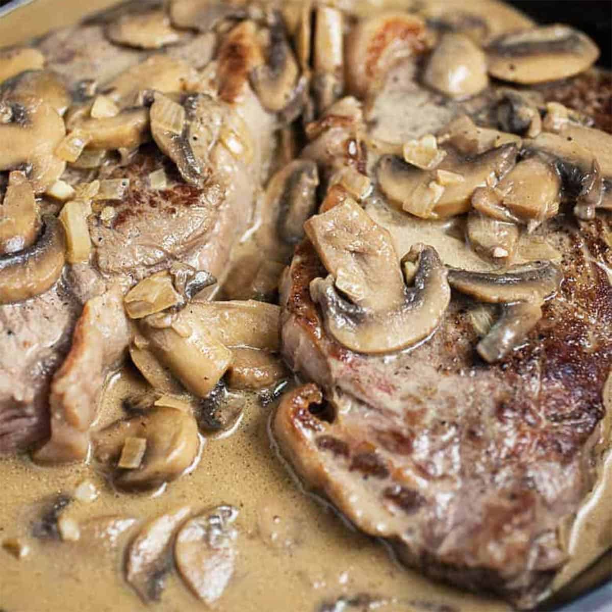 Diane sauce over steak in a skillet with mushrooms