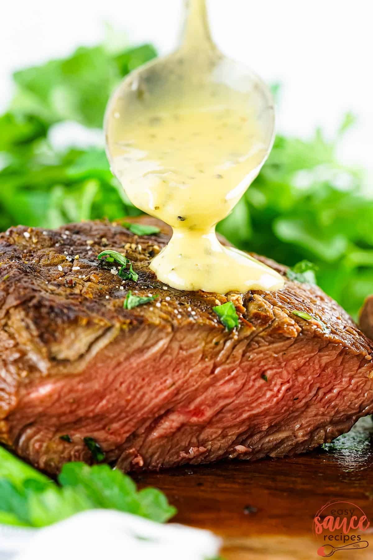 a steak, sliced side forward, with a spoon pouring bearnaise sauce on it and lettuce in the background