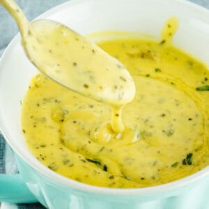 a spoon full of bearnaise sauce over a turquoise gravy boat filled with bearnaise sauce
