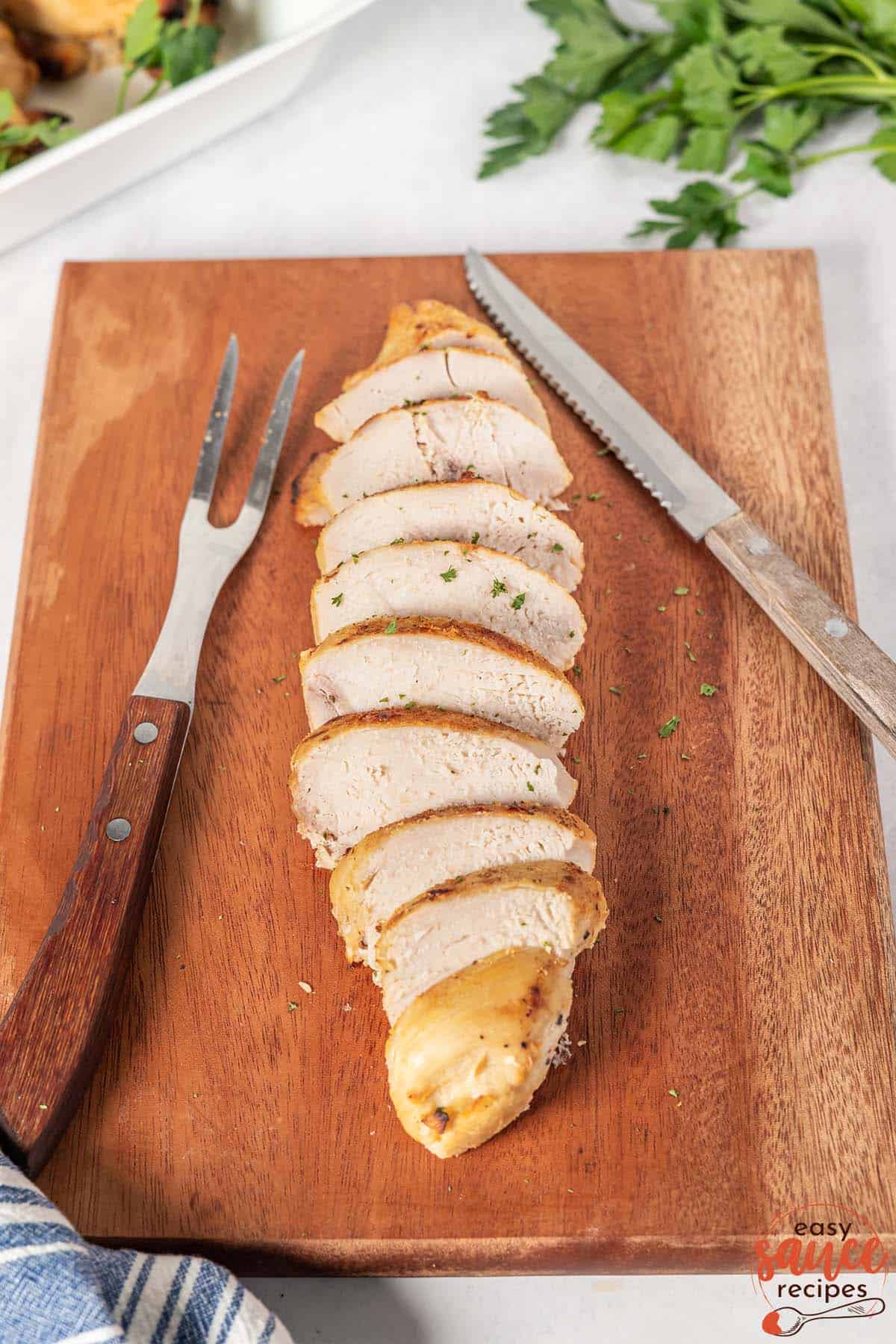 sliced chicken on a cutting board with a meat fork and knife