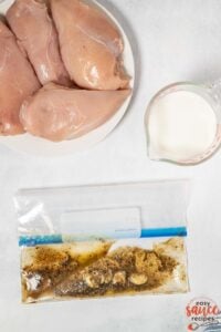 ziploc bag with buttermilk chicken marinade next to plate of raw chicken and measuring cup of buttermilk