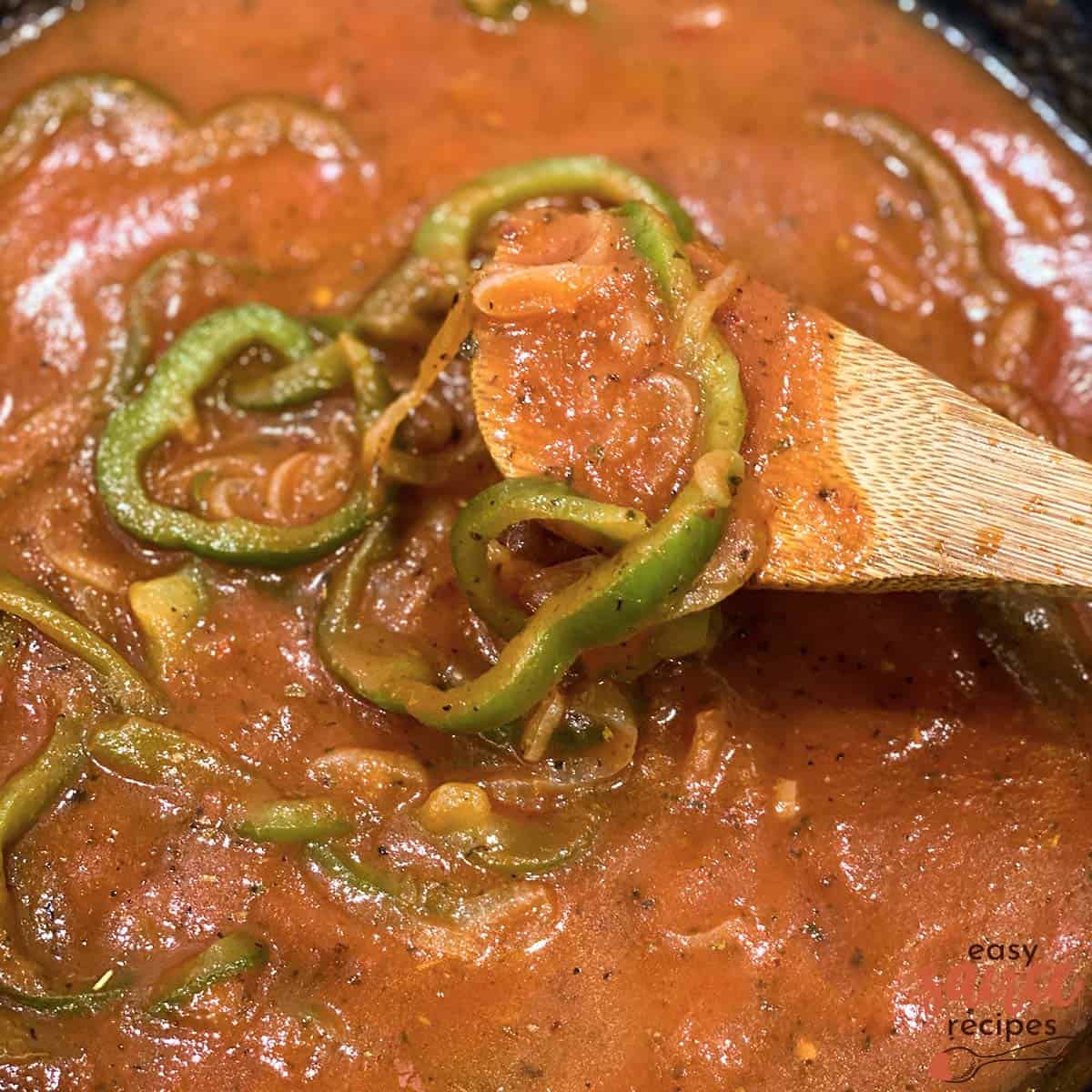 pizzaiola sauce on a wooden spoon over pan with bell peppers
