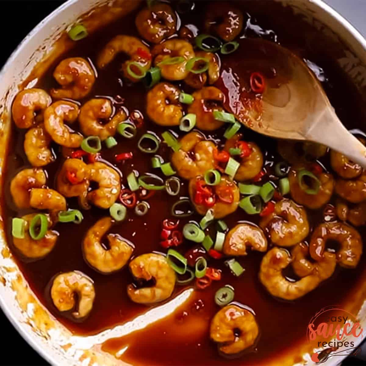 top view of a pan with sweet chili sauce, prawns, spring onions, and sliced red chilis