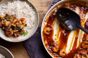 a bowl of rice and sweet chili sauce on prawns next to a pan of sweet chili sauce with prawns
