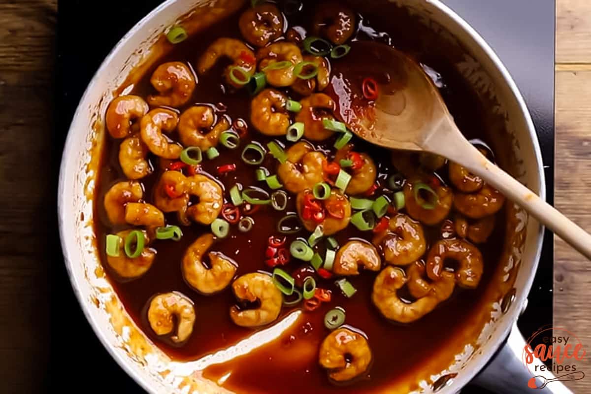 top view of a pan filled with prawns covered in sweet chili sauce, with spring onions and red chili peppers