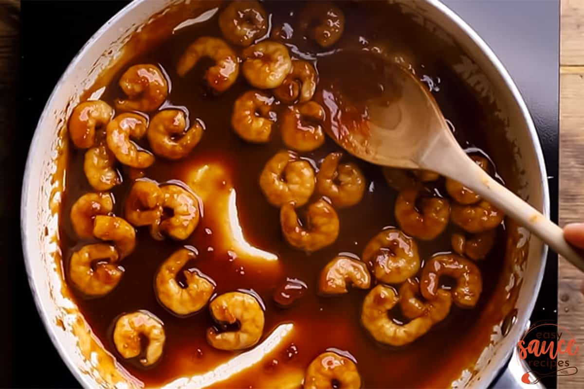 top view of a pan filled with sweet chili sauce and prawns, with a wooden spoon