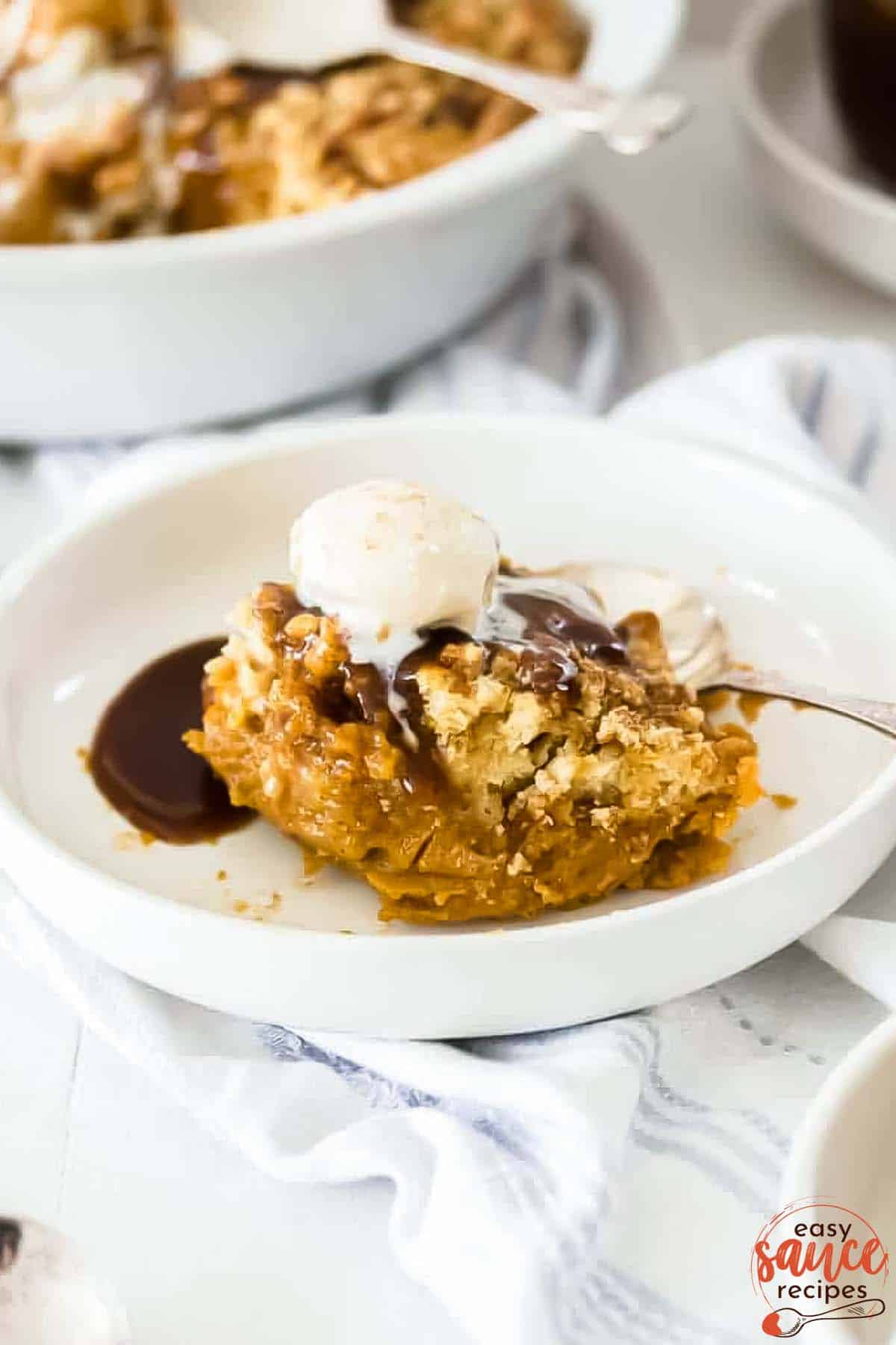 ice cream on top of a slice of pumpkin cobbler in a white dish with toffee sauce