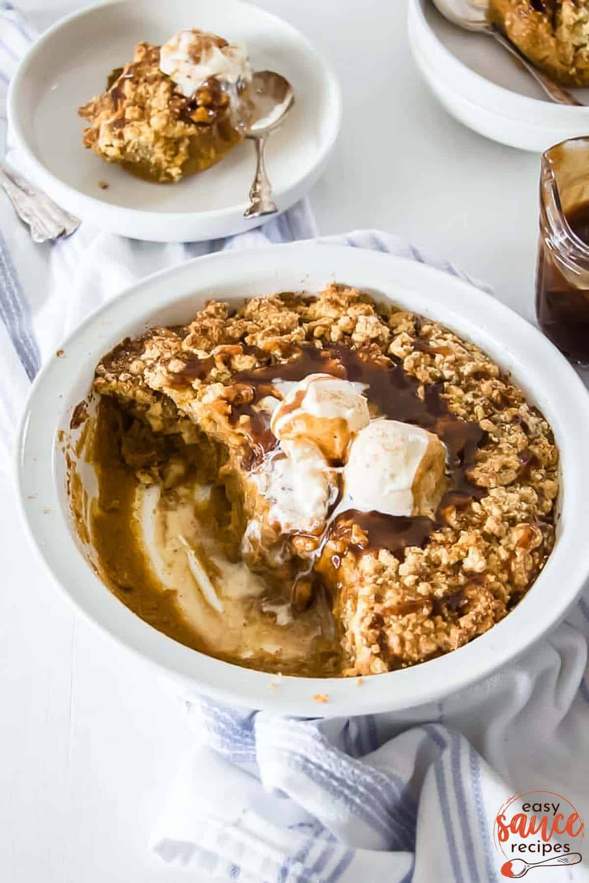 pumpkin cobbler in a white bowl with scoops of ice cream and toffee sauce on top