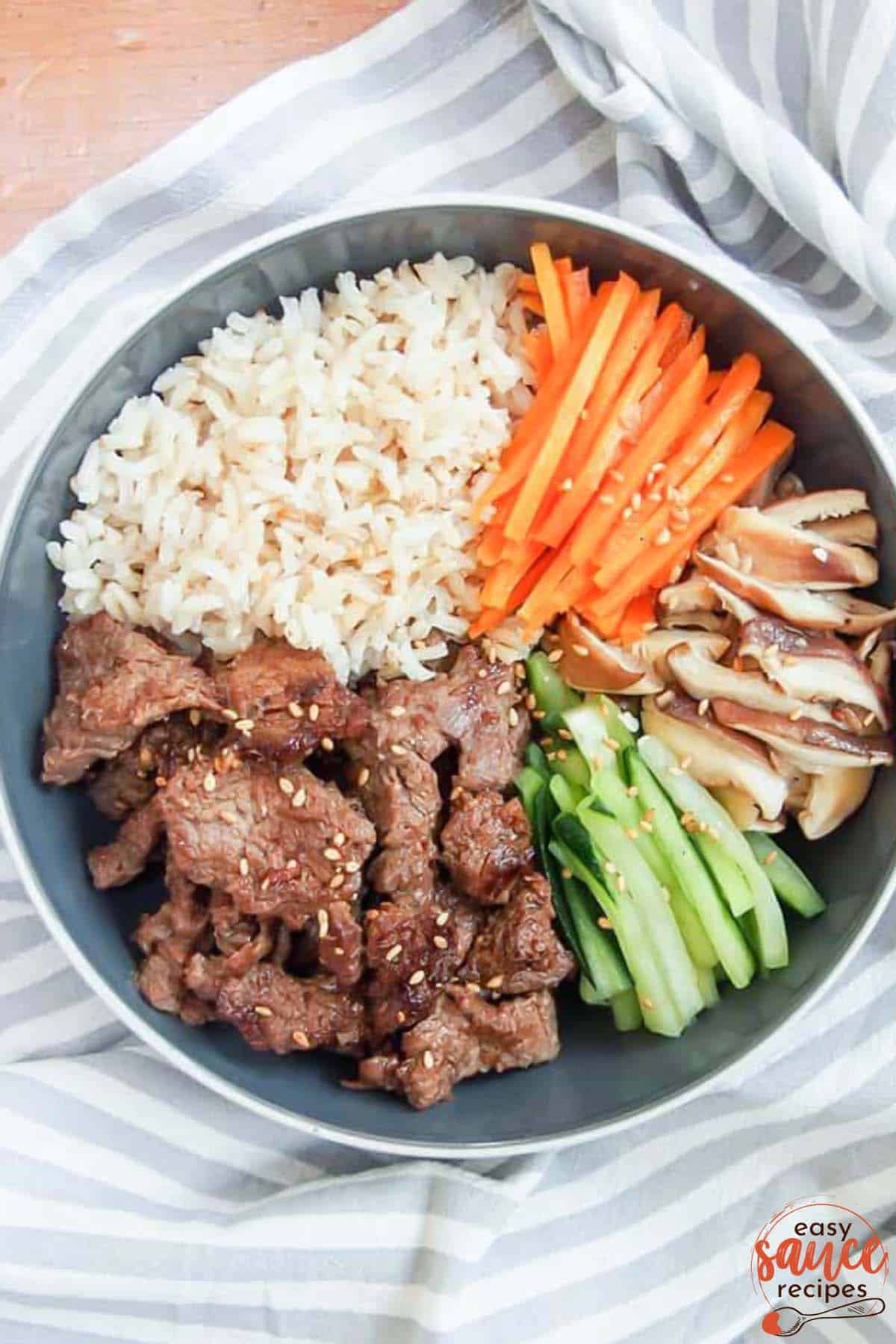 bulgogi marinated beef in a bowl with cucumbers, rice, carrots, and mushrooms